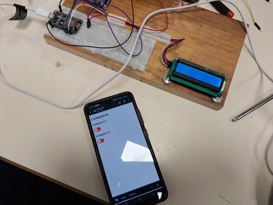 Esquema de conexión donde aparecen el Esp8266 conectado a un lcd por I2C y un modulo con dos reles conectados a lámparas a 220 volts y un celular que muestra una interfaz web con dos sliders que encienden y apagan las lámparas remotamente por una red wifi.