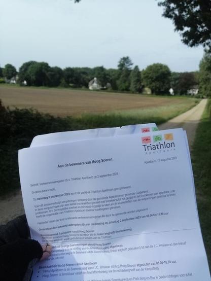 Holding up a letter with 'Triathlon Apeldoorn' logo with houses behind a field at the background