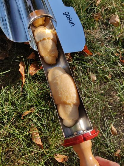 A vacuated-tube solar oven is sitting in some grass. The tray is pulled partway out to show crescent rolls turning puffy and flaky in the sun.