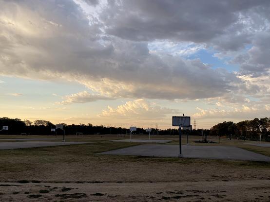 Levé de soleil sur un terrain de basket, la forêt à gauche, des nuages dans le ciel se colorent en orange.