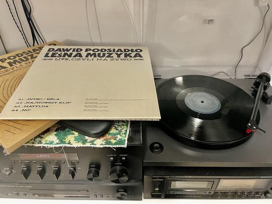 Zdjęcie przedstawia longplay - płytę winylowa na gramofonie. Obok okładka albumu Dawida Posiadło - Leśna Muzyka