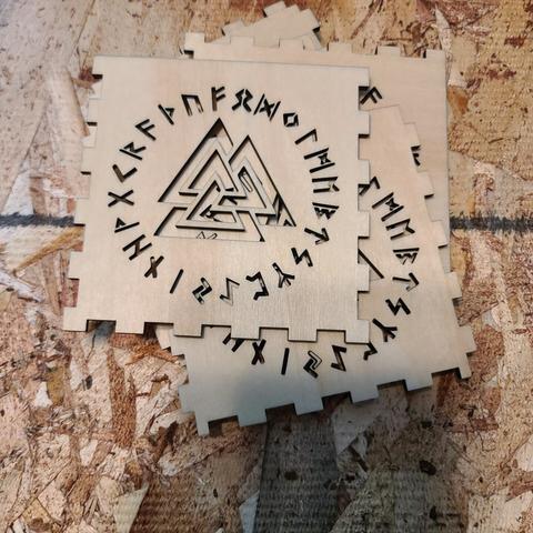 A pile of square, wooden tiles have runes and Norse symbols cut out of them. The edges of the tiles are shaped so that they can fit together like puzzle pieces. Together, they create a candleholder.