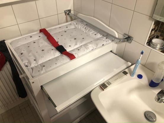 Auf dem Bild ist ein Wickeltisch zu sehen, mit einer Matratze und einem ausziehbaren Tisch.