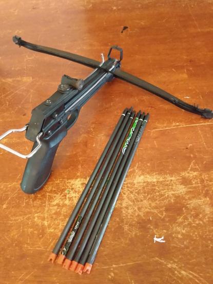 A pistol crossbow is shown next to 6 recycled crossbow bolts made by cutting down broken and discarded carbon fiber arrows from the range.