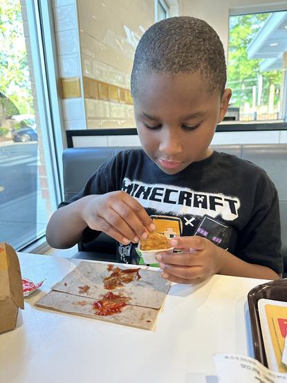 My son dipping a chicken nugget into barbecue sauce