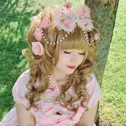 portrait picture of a woman with big brown hair and a pink dress, sitting and leaning against a tree with her eyes closed.