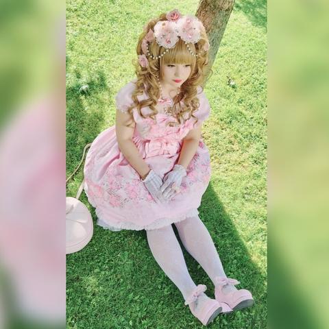 woman with with big brown hair and a pink dress sitting underneath a tree with her hands in her lap.