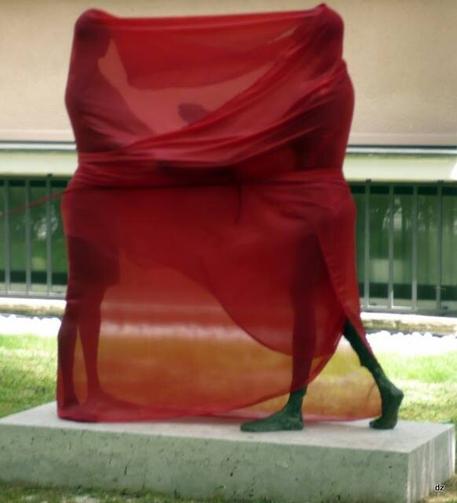 Kunstwerk: Zwei Menschen auf einem Betonsockel stehen sich gegenüber und sind mit rotem Tuch verhüllt.