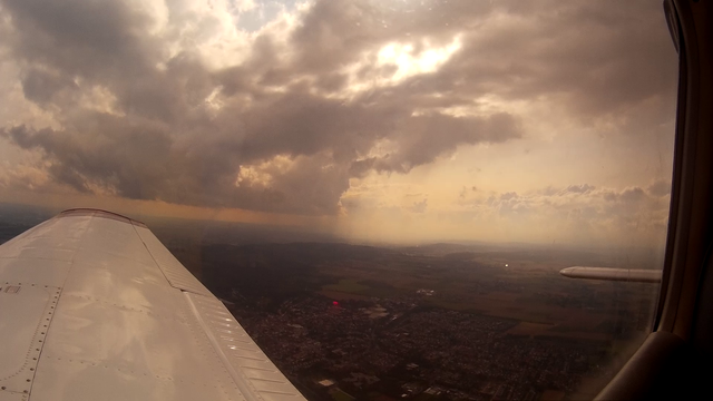 Aerial view of a rain cloud with a rain shower underneath and an airplane wing in view