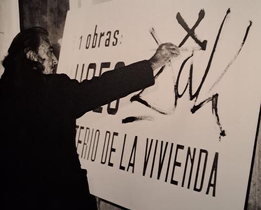 Salvador Dalí at an easel signing a signboard.