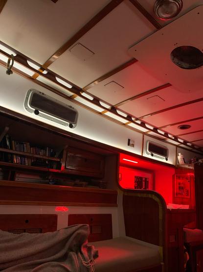 Blick in den Steuerbord Salon, von vorn nach hinten. Oben Fensterreihe in weiß, links unbeleuchtetes Bücherregal, rechts hinten Naviecke rot.