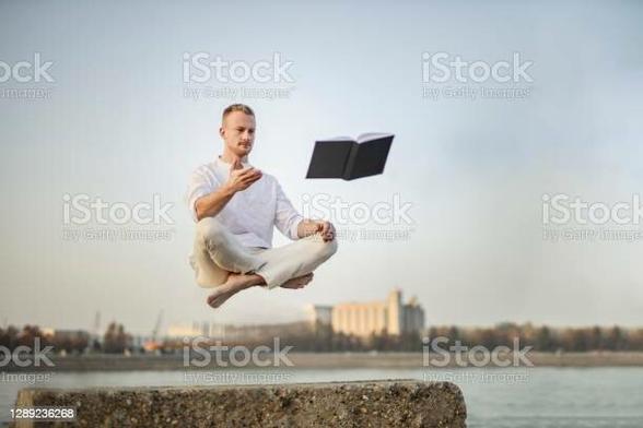 stock photo image of a man floating in the air in yoga position gesturing toward a floating book