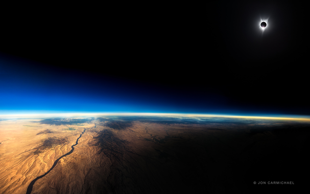 A black sky gives way to a blue dawn over planet earth. In the dark of space is a clear halo of the sun bursting behind the moon during a complete solar eclipse.