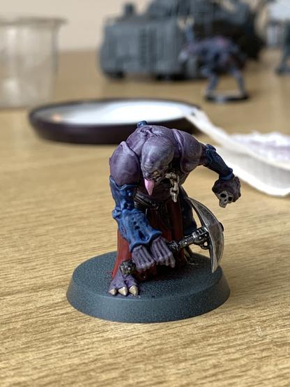 Close up of a Warhammer 40K Genestealer cult aberrant painted in the traditional purple and blue scheme. He’s holding a pick axe in two of his three arms; the other holds a skull.