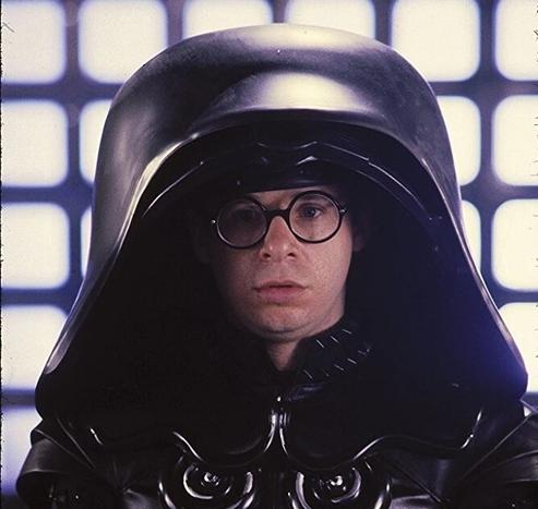 Screen cap from SpaceBalls with Rick Moranis playing a character named Dark Helmet that’s a paradox of Darth Vader, but with an enormous black helmet.