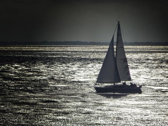 Monochrome photo of a small sailing boat against the light of the sunset on the Atlantic.