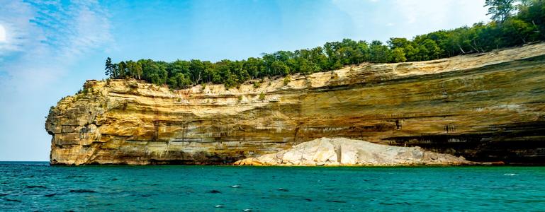 Pictured Rocks Panorama

This is a panoramic image of Pictured Rocks National Shoreline located on the south shore of Lake Superior just outside of Munising, Michigan.
The foreground os the image is the ice cold waters of Lake Superior. The water is a little choppy as seen with small white caps. 
The shoreline itself, in this area is a large cliff roughly 200 feet tall. In the right hand portion of the image there is a rock feature in the water that broke away from the cliffs. 
On top, the cliffs are covered in trees, pines and hardwoods both. 
The sky is cloudy and overcast near the outer edges of the image with a patch of blue sky mid image.