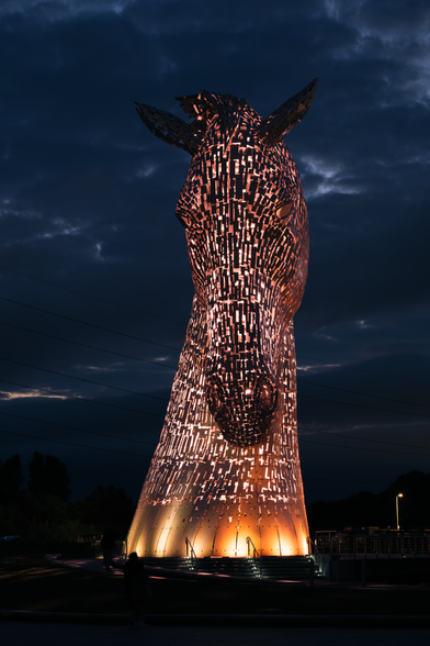 This is a photo of one of the two sculptures that make up The Kelpies, taken at The Helix in Falkirk, Scotland.

The sculpture is of a giant horse's head and neck, rising 30 meters in the air from the ground.

The image was taken as night fell, and it captures how the sculpture is designed to show all of the lighting inside it.