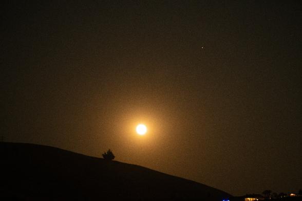 The blue supermoon shines in a smoky orange color above the hills.