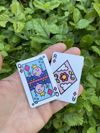 2 mini cards on my hand. The Queen of Diamonds is a little round pink creature with a crown, blowing bubbles. The ace of diamonds has a big pale pink diamond in the middle with clouds, leaves, and a flower.