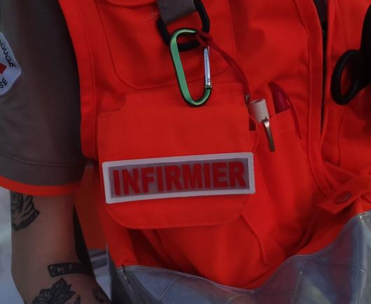 Gros plan sur une chasuble de la Croix-Rouge française avec un badge « Infirmier »