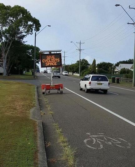 Photo shows a bicycle lane beside a busy road. The bicycle lane is blocked by a mobile traffic sign that advises motorists: 
GIVE CYCLISTS SPACE