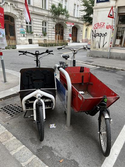 Zwei Lastenräder an einem Bügel festgemacht, der mit „Bitte hier für das Lastenrad freihalten“ beschriftet ist.