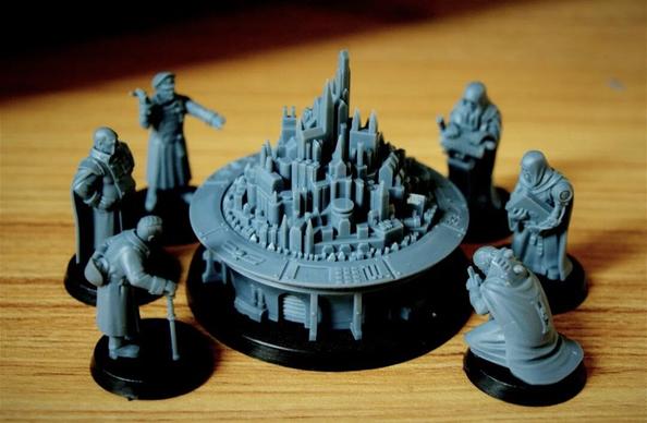 Photographie d'une scène avec des figurines imprimées en 3D de l'univers Warhammer 40000. Au centre, une figurine représentant la projection d'une ville façon hologramme, et autour 6 figurines représentant différentes personnes