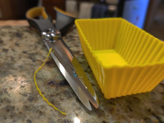 A small yellow rectangular silicone baking tray sits on a kitchen countertop. Next to it are a scissors and a thin strip of yellow silicone that has been trimmed from the upper long edge.