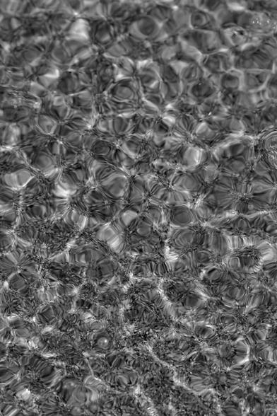 Boack and white portrait format image showing the beautiful reflections of sunlight in shallow water being rippled over sand by a gentle sea breeze at low tide
