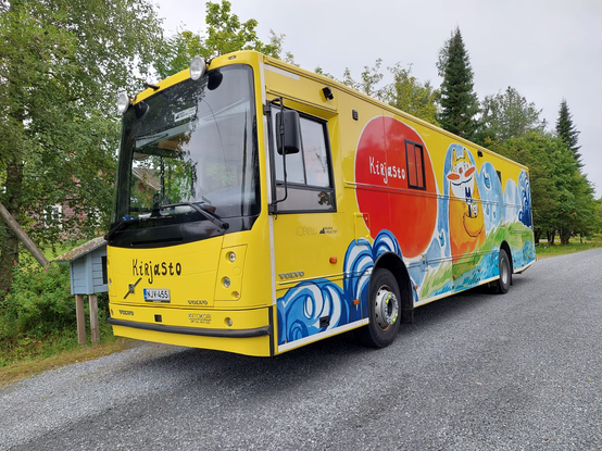 Valokuva kirjastoautosta. Värikkäästi koristellun auton kyljessä on mm. piirrettyjä kissahahmoja ja kirjoja sekä käsin kirjoitetun näköinen teksti ”Kirjasto”, pienemmällä myös Joensuun, Vaara-kirjastojen ja Volvon logot. Keulassa on sama ”Kirjasto”-teksti eri värillä kuin keulassa; lisäksi rekisteritunnus NJV-455, kolme Volvon logoa sekä Kiitokori Special Vehicles -logo.