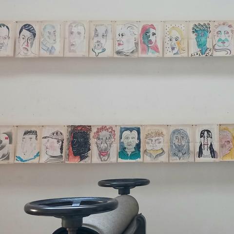 Eine Reihe von farbigen Portraits, gezeichnet auf Pspier, über einer Tiefdruckpresse.