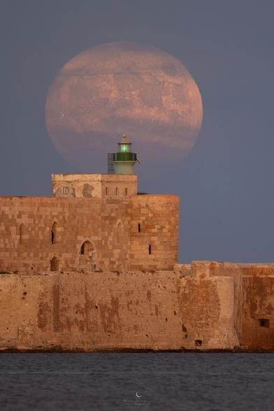 Moon photographed behind a lighthouse.