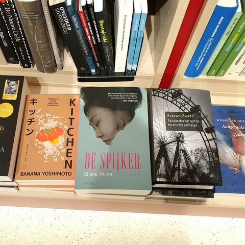 Foto van een stapel exemplaren van De spijker van Zhang Yueran, op het vlak voor de boekenkast, tussen boeken van Banana Yoshimoto en Stefan Zweig.