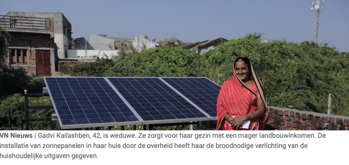 screenshot VN:
vrouw, lachend,  staat voor 3 zonnepanelen  die ze kreeg v.d. overheid, onder blauwe lucht
