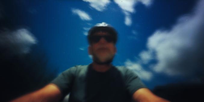 6x12 cm colour pinhole photo of a cyclist. The  camera mounted on the handlebars of the bike