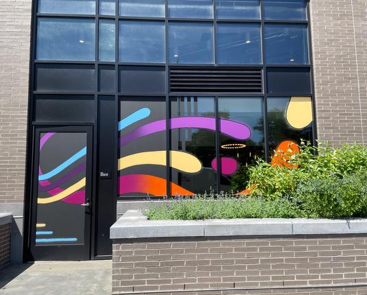 Painting of elongated curved lines in turquoise, lavender, yellow, pink, and orange suggesting a wave or spray of water emanating from a common point sprawls across a door and 4 large windows beside it. A small placard on the frame between the door and the first window read "Fire Command Center."