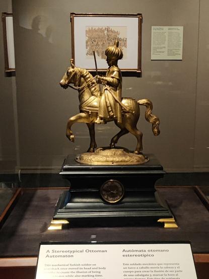 Generic Turkish figure with a turban on a horse, gilt, in front of a ragged sheet of playing cards on the wall.