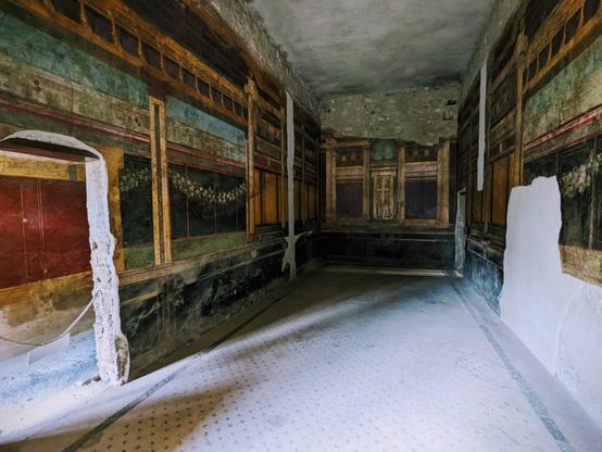 This is a long room with large, vibrant frescas on every wall.  The floor has tiles.  In the lower left-hand corner is a door going to the next room.  A rope stretches across the doorway.