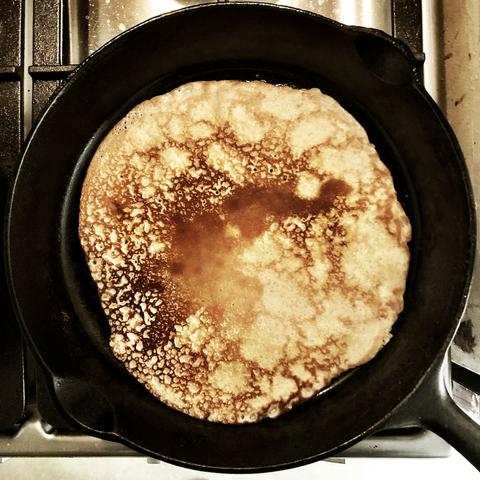 Colour photo of a cast iron frying pan with a cooked pancake in it.