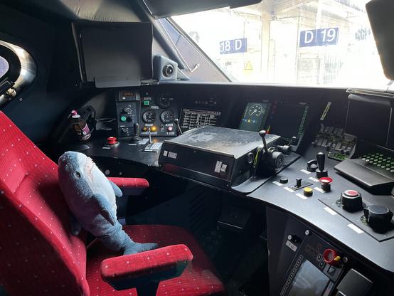 Blåhaj sitzt auf dem roten Stuhl im TGV Führerstand