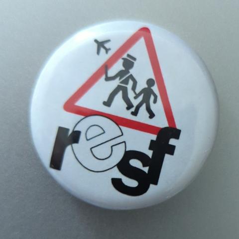 badge RESF, un panneau d'interdiction triangle rouge, avec deux personnages en noir, un gendarme qui tient un enfant par les menottes et qu'il emmène vers un avion, les lettre resf sous le panneau.