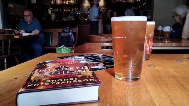 Foreground showing book and pints of ale on table, background of the interior of Cloisters pub on a warm afternoon