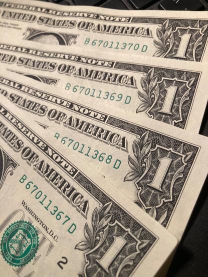 A sequence of four serial numbers are pictured on four one dollar US bills.