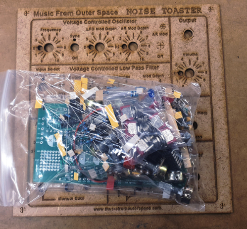 Bolsa de compoñentes electrónicos enriba dunha plancha de DM de 3mm cortado con láser. Na plancha pódese leer Music From Outer Space. NOISE TOASTER