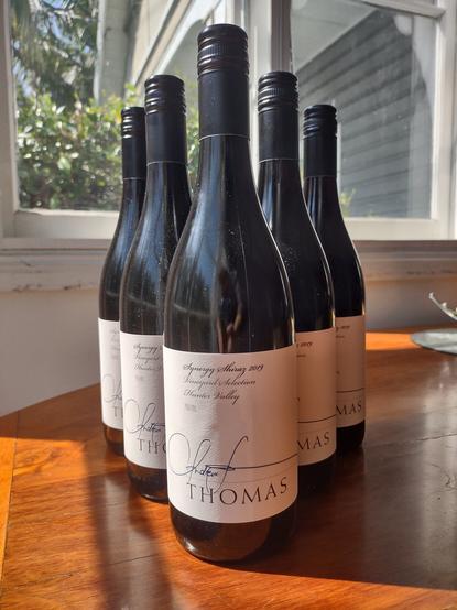 6 bottles of Andrew Thomas 2019 Synergy Shiraz arranged in a phalanx sitting on a wooden table