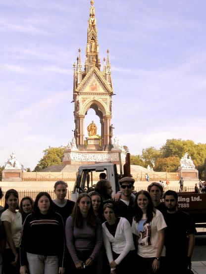 12 college students who flew overnight from the United States and who have still not gone to sleep by the time this photo was taken at 9:45 a.m. pose across the street from the Albert Memorial in Kensington Gardens. 11 of the students face the camera, but yours truly has turned to look intently at something out of frame to his left. This photo is poorly exposed with the subjects in shadow and the background in bright sunlight.