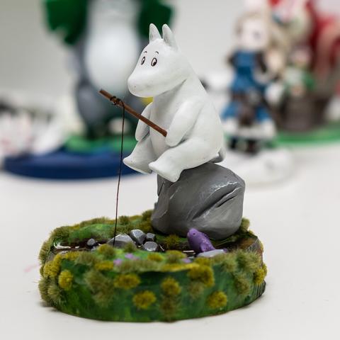 A moomin sitting on a rock, fishing in a small stream, Clayfigure, about 12cm high on a woodenbase. Details see post.