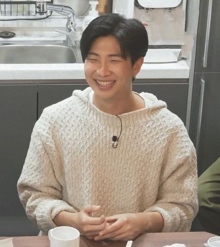 Namjoon in a cuddly white sweater, smiling so hard his eyes have disappeared