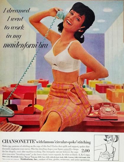 A women sits on a desk with a skirt and not top, other than her cone bra. She is talking on a telephone